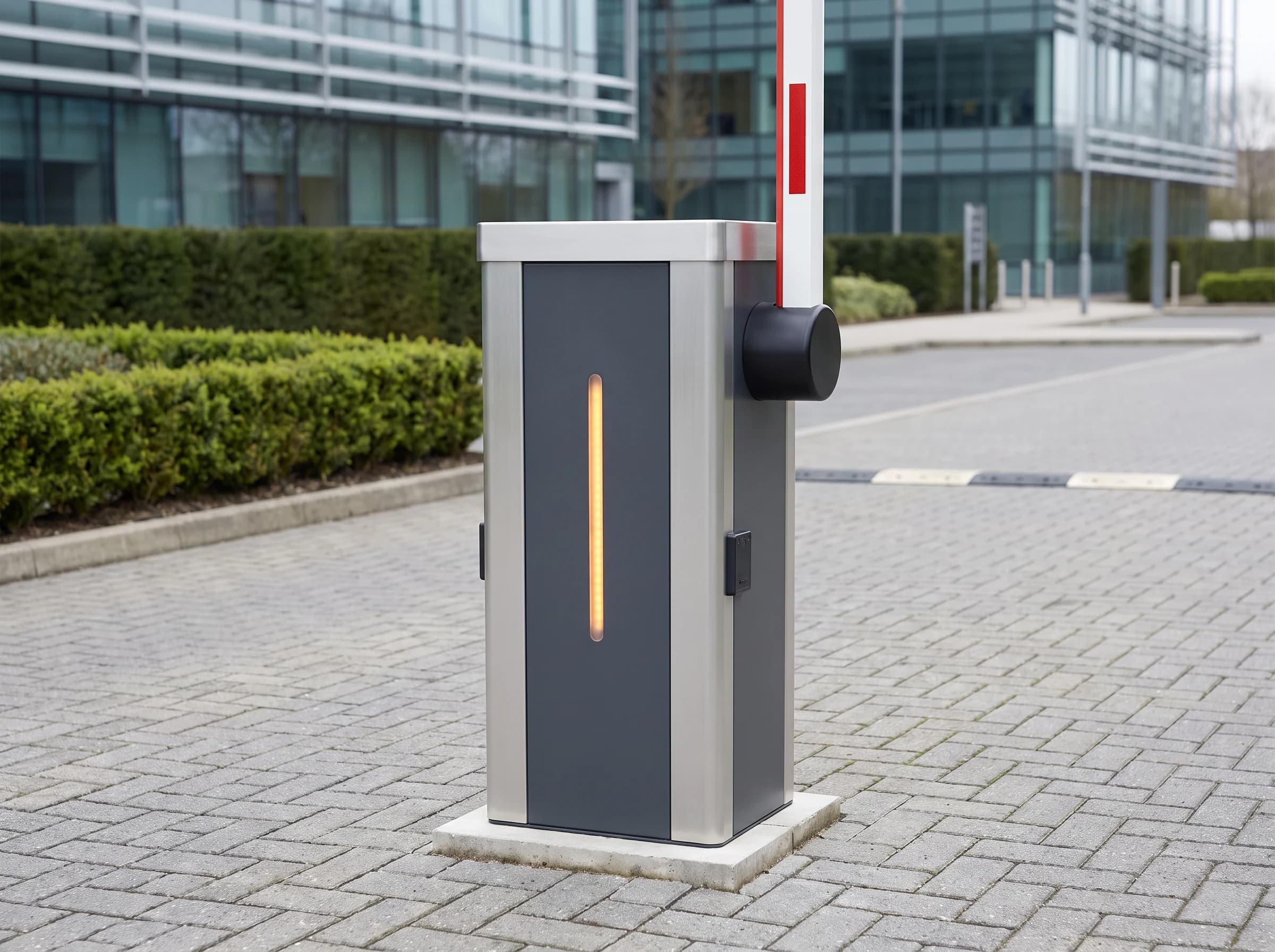 An automatic boom barrier seen from across the lane with its arm raised vertical beside the cabinet: a graphite-grey pedestal with brushed silver side panels, an amber status strip on the front face, a reader plate on the side and a black boom boss carrying the white and red arm