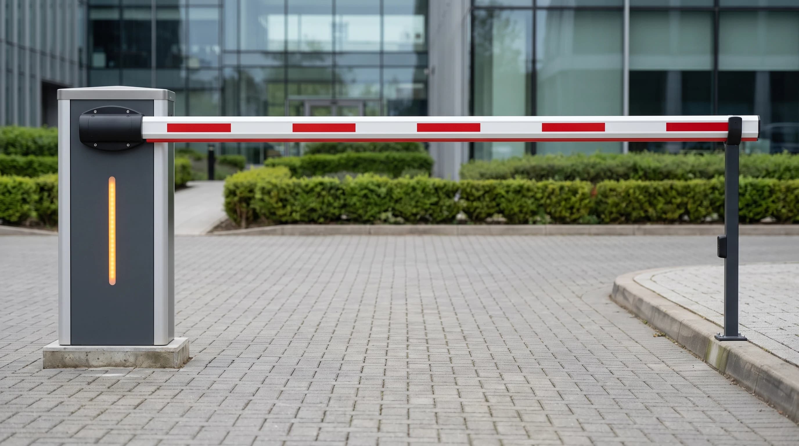 Side elevation of a boom barrier with its arm horizontal across the lane: the graphite-grey cabinet with brushed silver side panels and amber status strip at the left, the white arm with evenly spaced red reflective bands, and a black tip support post at the far kerb