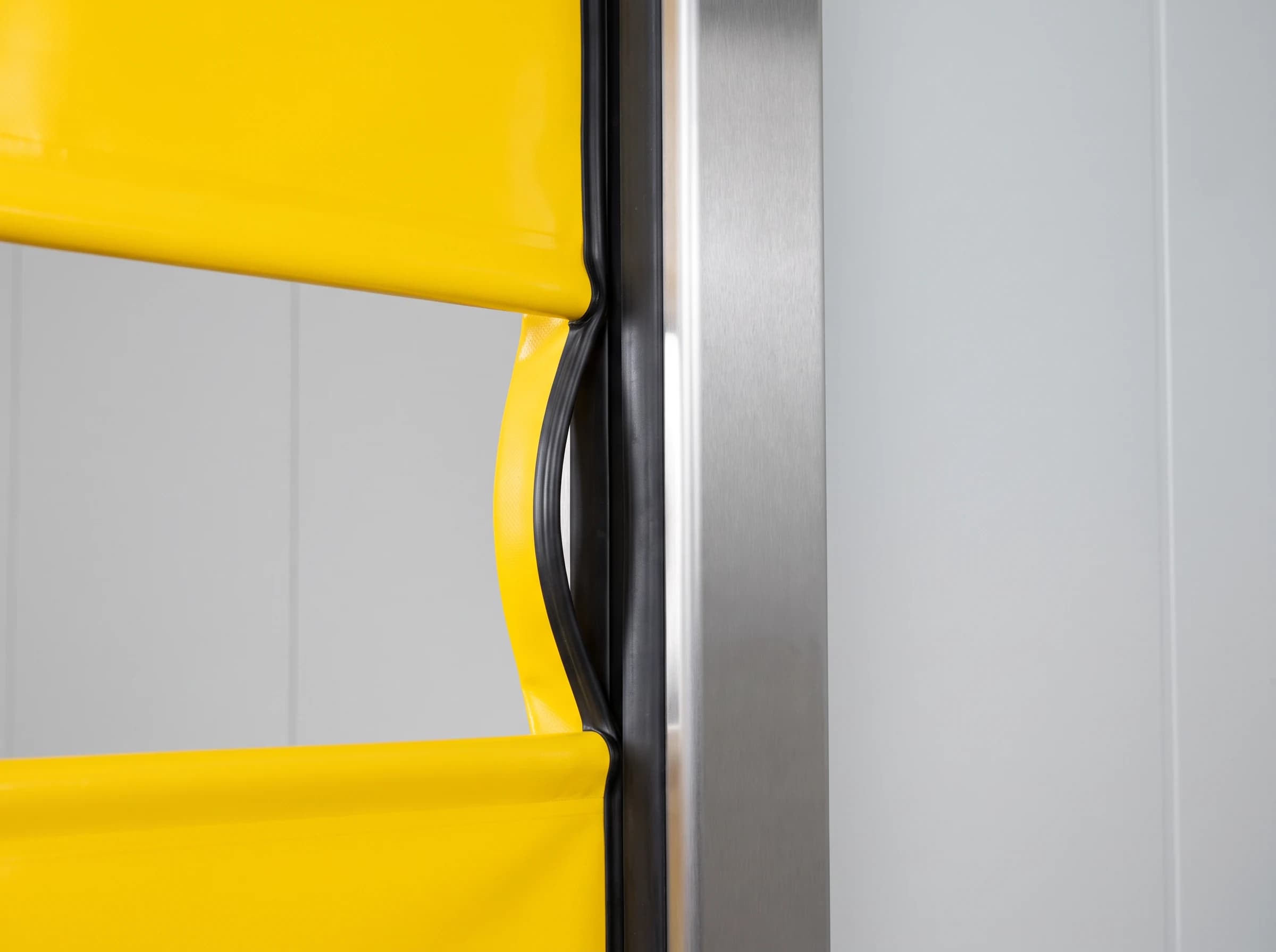 Close-up of the self-repairing guide of a high speed door: the yellow curtain's edge bead has released from the black flexible channel in the stainless guide over a short section after impact, the curtain bowing away undamaged while above and below the bead remains seated